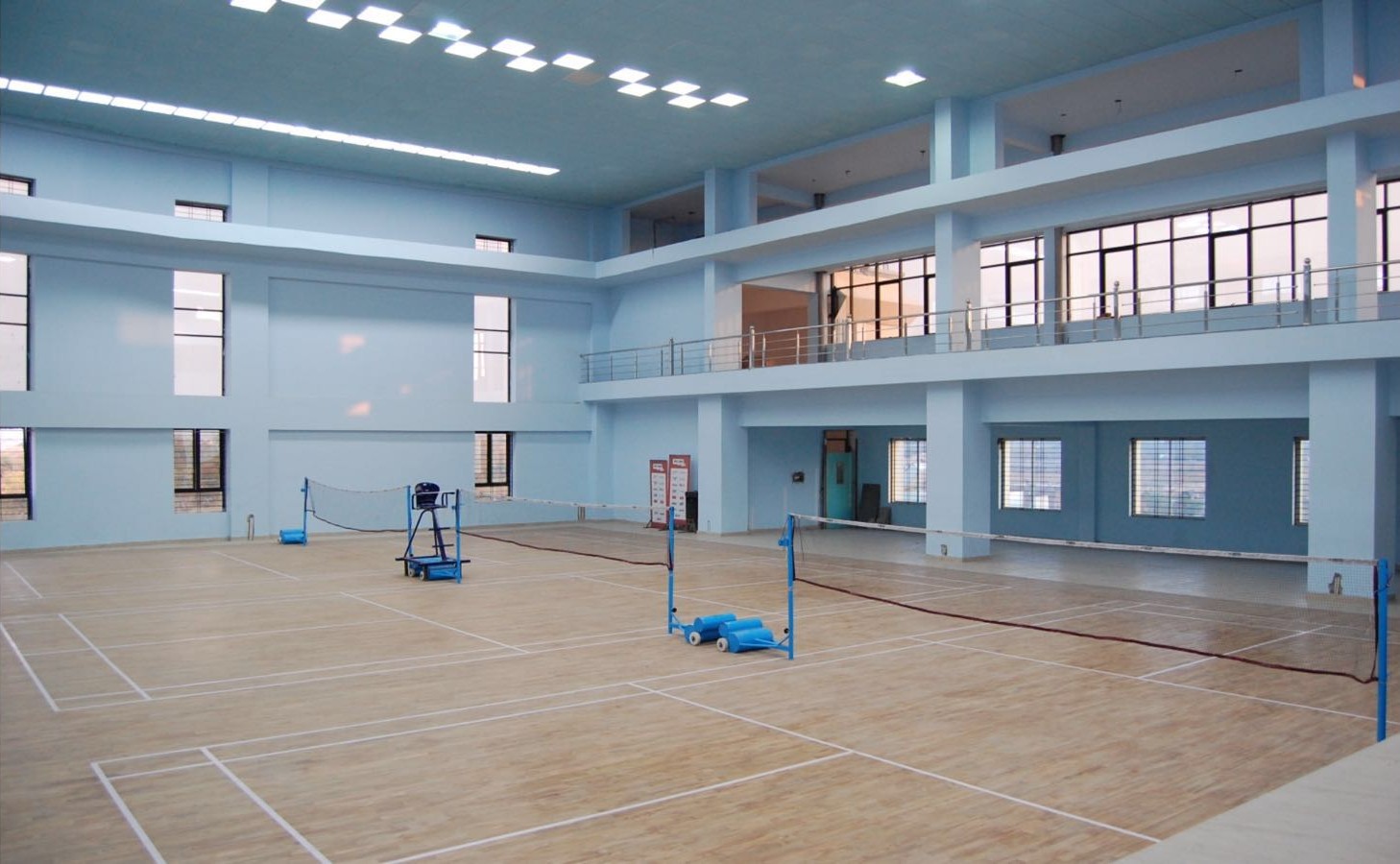 Indoor badminton hall with marked courts, nets and a wooden floor at a school in India